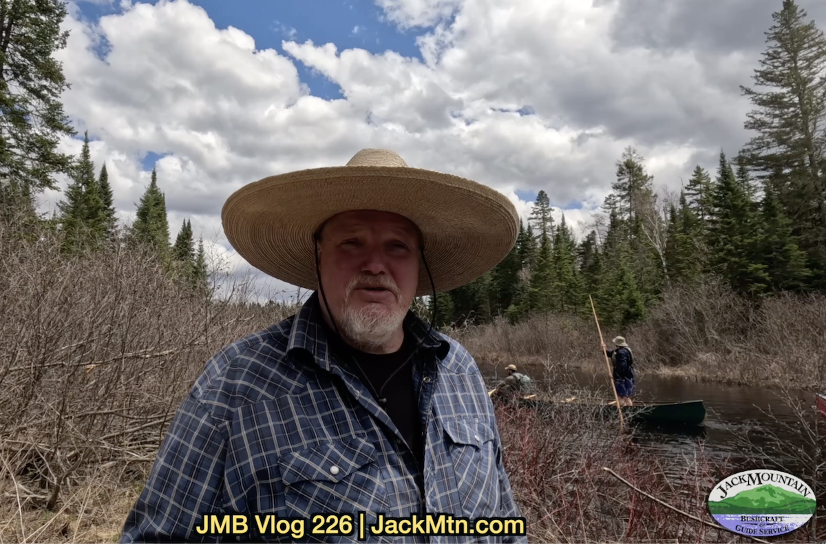 Tim standing by the stream with people poling canoes in the background