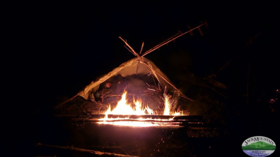 a small shelter next to a long fire, no sleeping bag