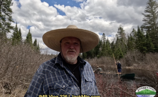 Tim standing by the stream with people poling canoes in the background