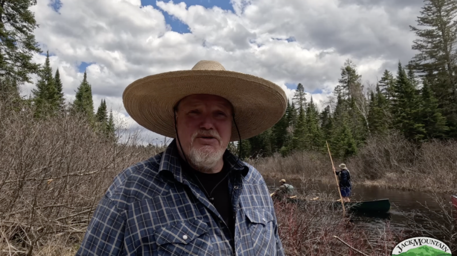 Tim standing by the stream with people poling canoes in the background