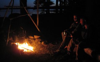 sitting by a campfire at dusk on a Maine lake
